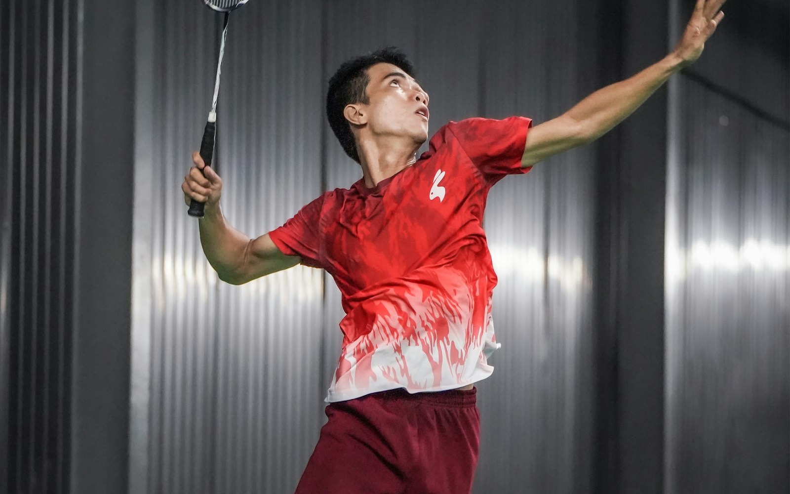 A badminton player jumping to hit a shuttlecock on an indoor court