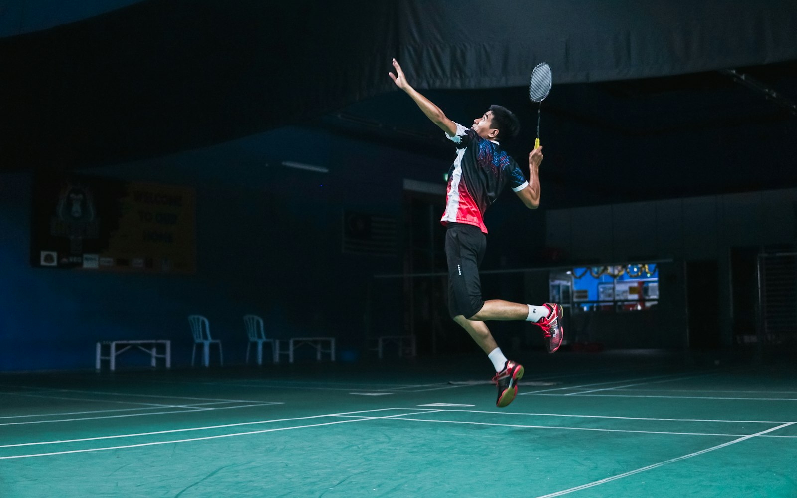 A badminton player jumping to play a shot on an indoor court